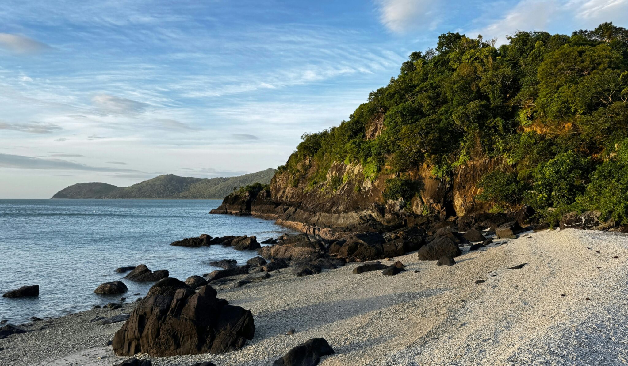 a sandy beach next to the ocean under a blue sky