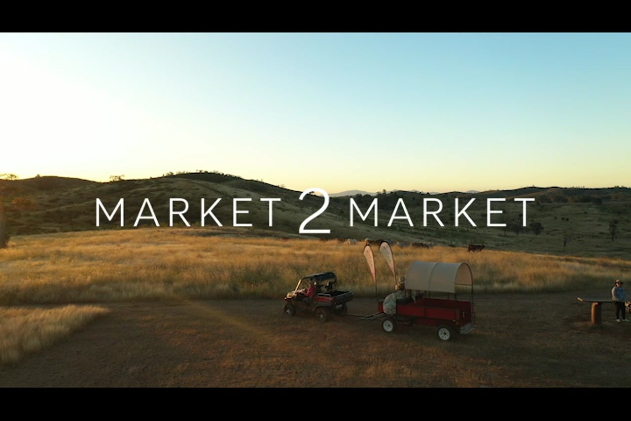 Aerial footage tracking along with small kubota and trailer driving through rural property at dusk.