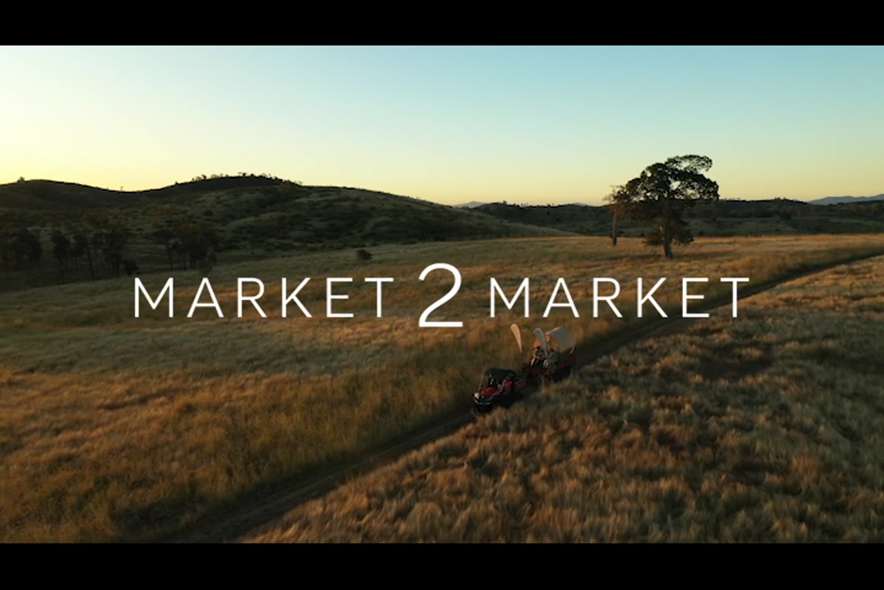Aerial footage tracking along with small kubota and trailer driving through rural property at dusk.