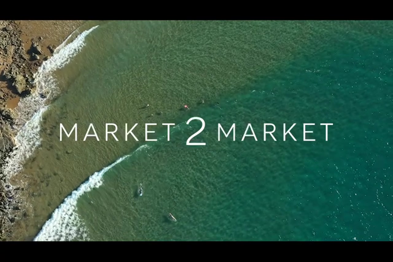 Aerial footage of surfers from overhead at beach with a rocky coastline