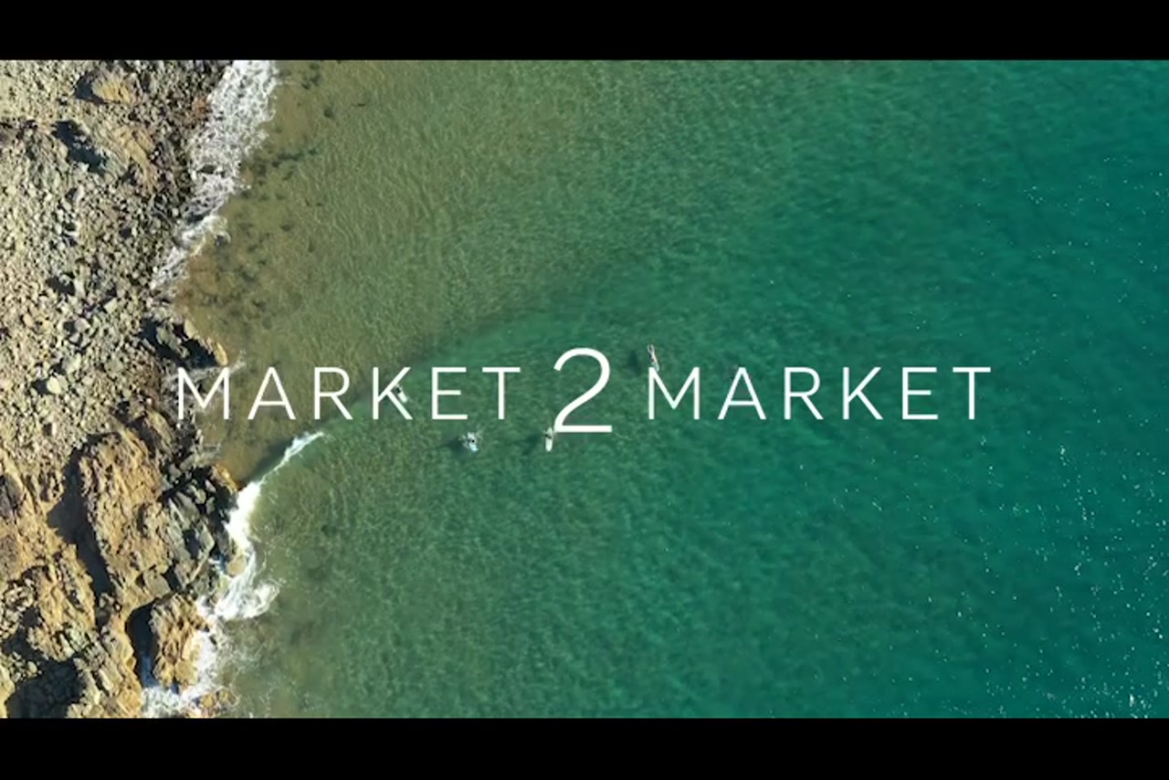 Aerial footage of surfers from overhead at beach with a rocky coastline